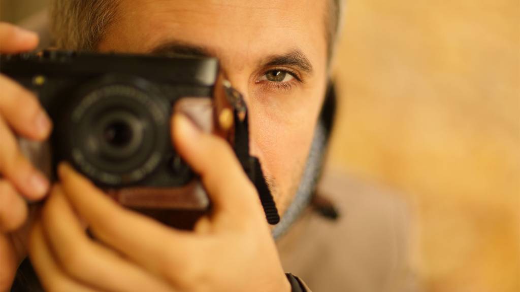 Primer plano hombre sosteniendo una cámara de fotografía en el momento de colocar su ojo en la mira para apuntar y realizar la fotografía.