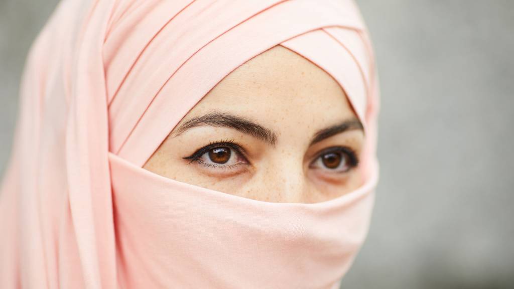 Mujer tapado con un hiyab de color rosa clara a la que se le ven solo los ojos marrones y las cejas